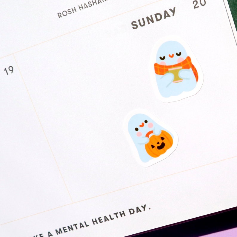 May include: Two cute ghost stickers with a white background. One ghost is holding a pumpkin and the other is holding a cup of coffee with a scarf around its neck.