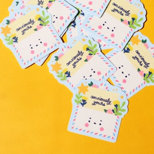 Pode incluir: Um monte de adesivos de envelope azuis e brancos com um rosto de desenho animado fofo e o texto "anxiously yours" em escrita preta. Os adesivos s&atilde;o decorados com estrelas amarelas, flores rosa e amarelas e folhas verdes.
