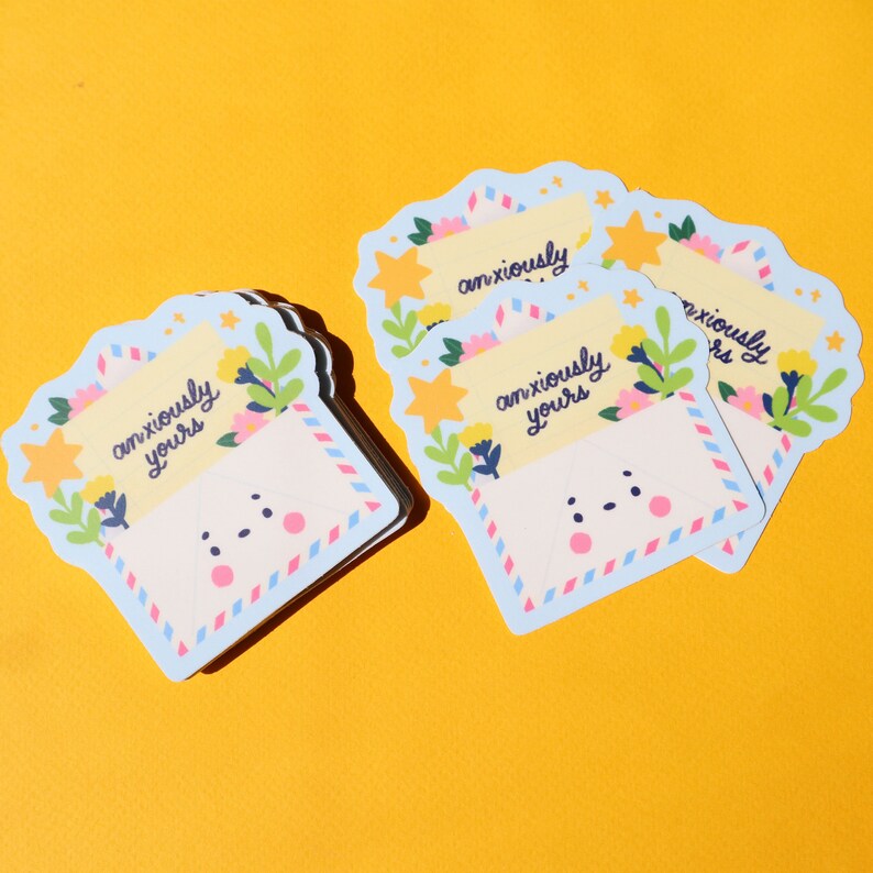 Pode incluir: Quatro adesivos de envelope azul e branco com um rosto de desenho animado fofo e o texto "anxiously yours" em amarelo. Os adesivos t&ecirc;m um design floral com estrelas amarelas e flores cor-de-rosa.