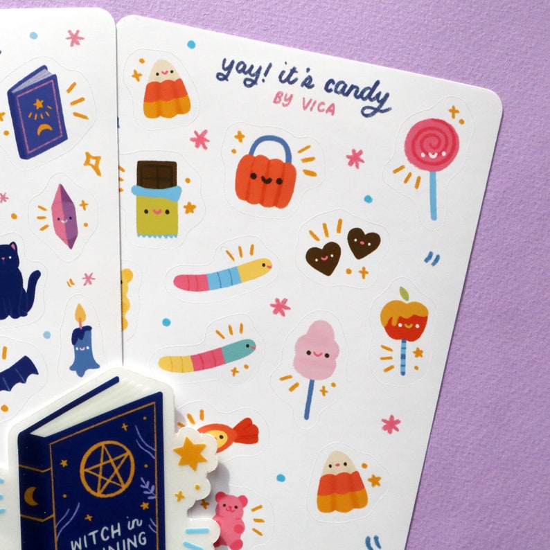 May include: A sheet of stickers featuring various Halloween-themed candy designs. The stickers are white with colourful illustrations of candy corn, lollipops, chocolate bars, gummy worms, and more. The text "yay! it's candy by VICA" is written at the top of the sheet.