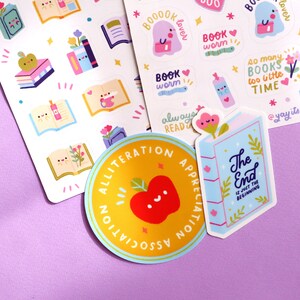May include: A set of colourful stickers featuring book-themed illustrations and text. The stickers include a red apple with a face, a book with the text "The End is just the beginning", and a ghost with the text "Book lover".