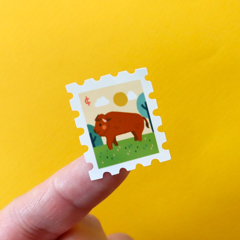 May include: A white sticker with a brown bison standing in a green field. The sticker has a white border with a scalloped edge and the text "&cent;" in red.