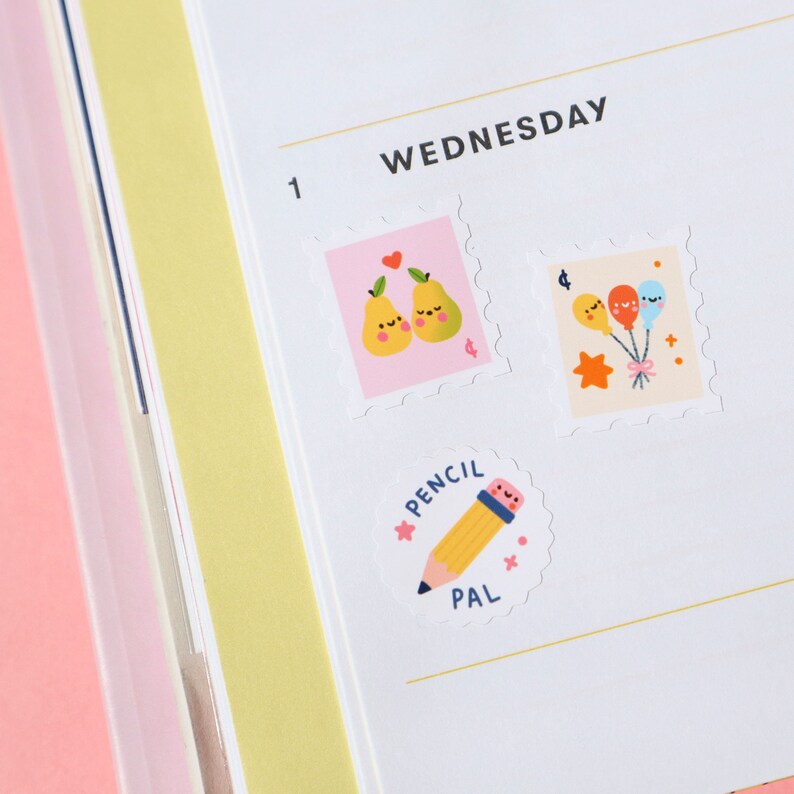 Pu&ograve; includere: Una pagina di un planner con la parola "MERCOLED&Igrave;" scritta in alto. Ci sono tre adesivi sulla pagina: un adesivo rosa con due pere, un adesivo con tre palloncini e un adesivo con una matita che dice "PENCIL PAL".