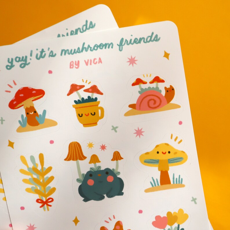 May include: A sheet of stickers featuring cute mushroom-themed illustrations. The stickers include a mushroom with a face, a snail with a mushroom shell, a frog, and a mushroom with a face in a pot. The sheet is titled "yay! it's mushroom friends by VICA".