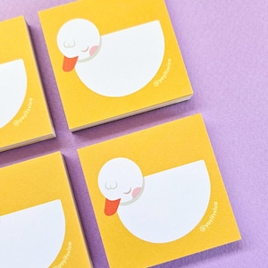 May include: A set of square sticky notes with a yellow background and a white duck illustration. The duck has a small orange beak and pink cheeks. The text @yayitsvica is printed in white on the lower right side of each square note.
