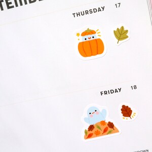 May include: Two stickers featuring fall-themed illustrations. The first sticker shows a pumpkin with a smiling face wearing a blue hat. The second sticker shows a blue bird perched on a pile of autumn leaves.