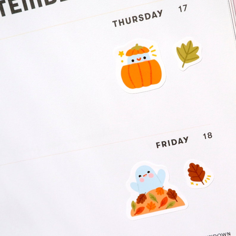 May include: Two stickers featuring fall-themed illustrations. The first sticker shows a pumpkin with a smiling face wearing a blue hat. The second sticker shows a blue bird perched on a pile of autumn leaves.