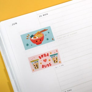 Op de afbeelding: Twee kleurrijke stickers met illustraties van eten. De eerste sticker is blauw en heeft een kom ramen met eetstokjes. De tweede sticker is roze en heeft twee kopjes boba-thee met de tekst "BOBA BUDS".