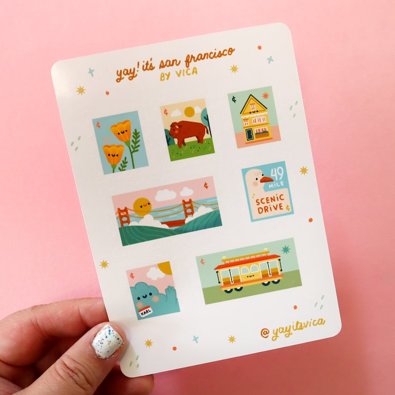 May include: A sheet of stickers featuring illustrations of San Francisco landmarks, including a cable car, a seagull, a house, a Golden Gate Bridge, a flower, and a buffalo. The stickers are on a white background with a pink border and the text "yay! it's san francisco by vica" at the top.