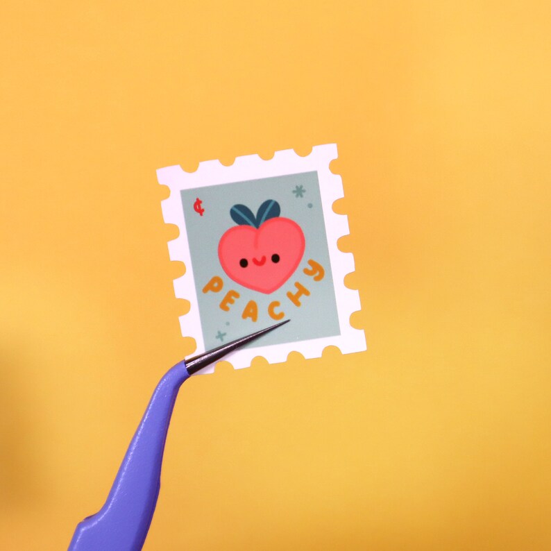 Op de afbeelding: Een sticker in de vorm van een perzik met een glimlachend gezicht en het woord "Peachy" in een speels lettertype. De sticker is op een witte achtergrond met een decoratieve rand.