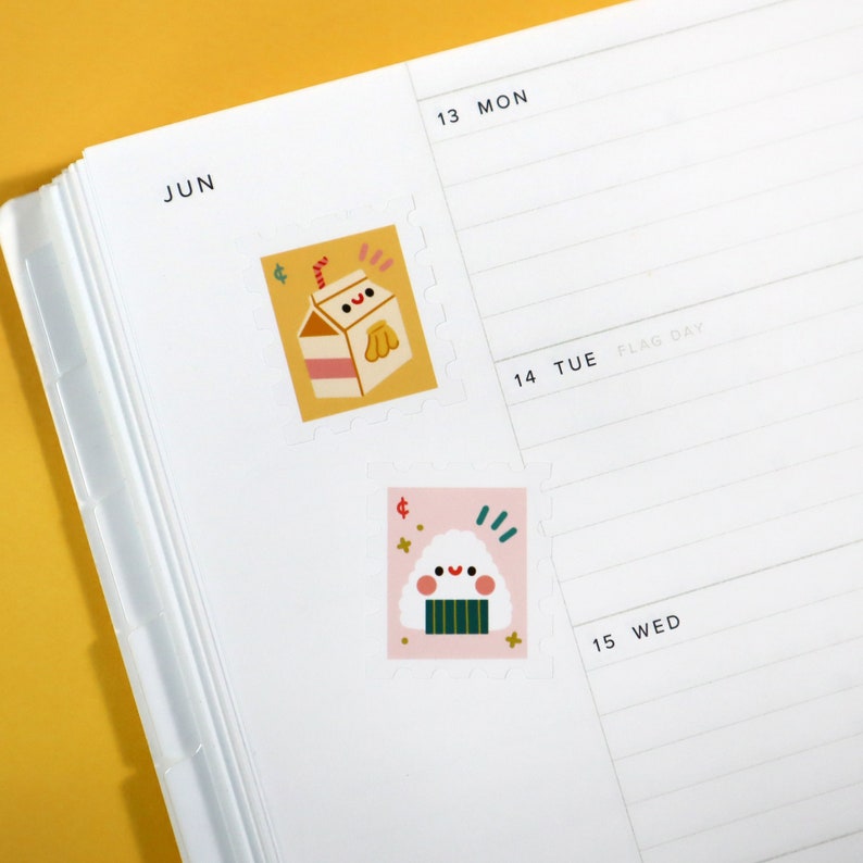 Op de afbeelding: Twee kleurrijke stickers met cartoonfiguren op een witte plannerpagina. De eerste sticker is geel en heeft een cartoonmelkpak met een rietje en een glimlachend gezicht. De tweede sticker is roze en heeft een cartoononigiri met een glimlachend gezicht. De plannerpagina heeft bovenaan het woord "JUN" en de dagen van de week staan eronder vermeld.