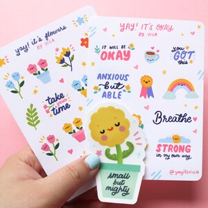 May include: A set of colorful stickers with positive affirmations and cute illustrations. The stickers feature phrases like "It will be okay", "You got this", "Breathe", and "Strong in my own way". The illustrations include a flower, a rainbow, a cup of tea, and a sun.