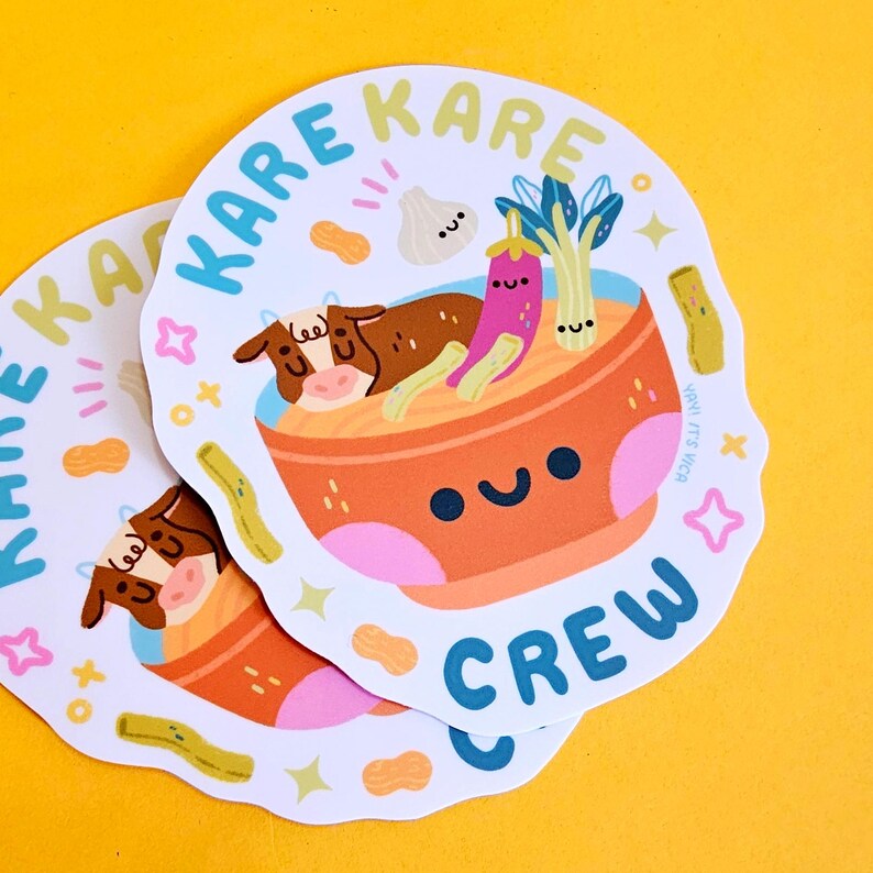 K&ouml;nnte beinhalten: Zwei wei&szlig;e Aufkleber mit einer Cartoon-Illustration einer Sch&uuml;ssel Kare Kare mit einer Kuh, Erdn&uuml;ssen, Knoblauch, Aubergine und Fr&uuml;hlingszwiebeln. Der Text "Kare Kare Crew" ist in blauer, gr&uuml;ner und gelber Schrift um die Sch&uuml;ssel herum geschrieben.
