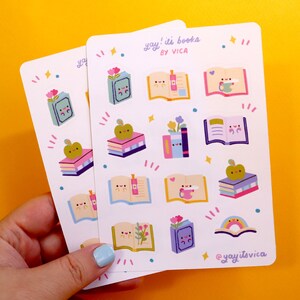 May include: A sheet of stickers featuring cute illustrations of books with faces. The stickers are on a white background with colourful accents. The text on the sheet reads "yay! it's books by VICA" and "@yayitsvica".