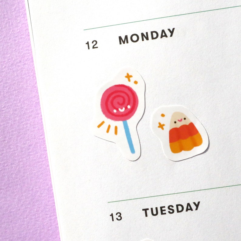 May include: Two Halloween themed stickers, one with a pink and white lollipop with a blue stick and the other with a smiling orange and yellow candy corn.