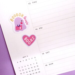 May include: A calendar page with a pink heart sticker that says "BOOKS" and a purple ghost sticker that says "BOOOK lover". The calendar is for May and shows the dates 1-29.