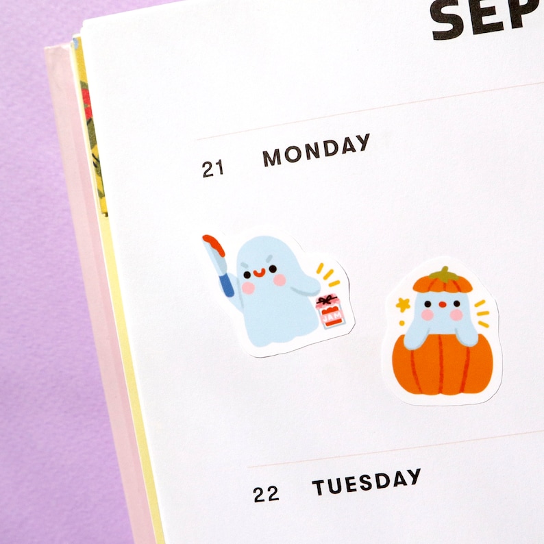 May include: Two Halloween themed stickers. The first sticker features a white ghost holding a knife and a box of candy. The second sticker features a ghost wearing a pumpkin hat and sitting inside a pumpkin.