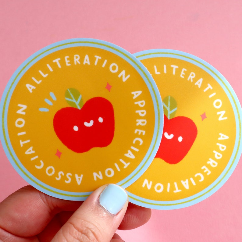 May include: Two yellow and blue round stickers with a red apple and the text "Alliteration Appreciation Association" on them.