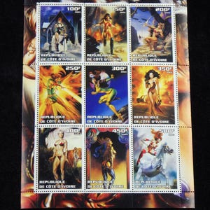 May include: A sheet of nine postage stamps featuring illustrations of women in various fantasy settings. The stamps are from the Republic of Côte d'Ivoire and feature the text "JULIE BELL" at the top. The stamps are valued at 100F, 150F, 200F, 250F, 300F, 350F, 400F, 450F, and 500F.