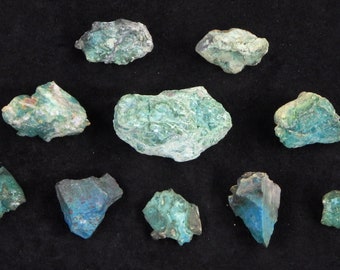 May include: A collection of ten green and blue stones, some with a rough texture, on a black background.