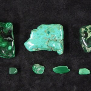 May include: A collection of seven green malachite stones of varying sizes and shapes. The stones have a swirling, marbled pattern.