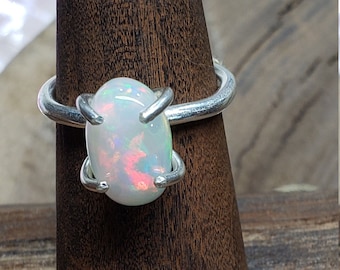 May include: A silver ring with a white opal gemstone. The ring is set on a wooden ring display stand.