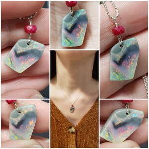 May include: A silver chain necklace with a black and iridescent opal pendant and a red gemstone accent. The opal has a swirling pattern of colors, including pink, green, and blue.