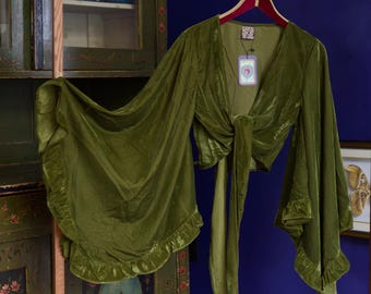 May include: An olive green velvet tie-front top featuring long, wide bell sleeves with ruffled cuffs. The garment has a deep V-neckline and a long fabric tie at the centre. A brand tag with an eye graphic and text is attached to the neckline.