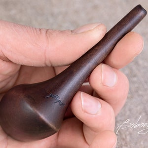 May include: A dark brown wooden tool with a rounded end and a pointed tip. The tool is engraved with the word "Bobonych".