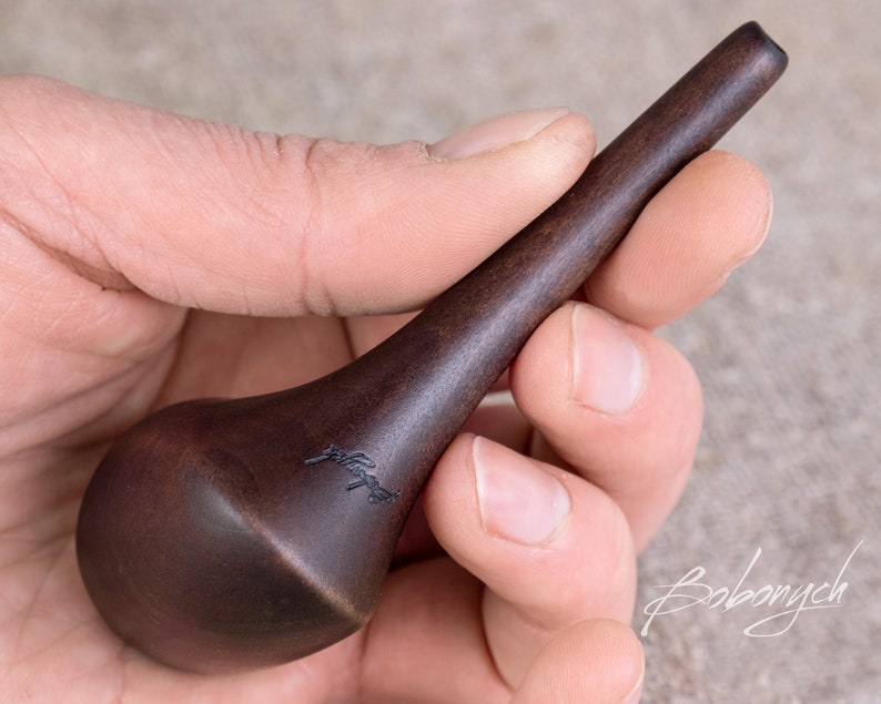 May include: A dark brown wooden tool with a rounded end and a pointed tip. The tool is engraved with the word "Bobonych".