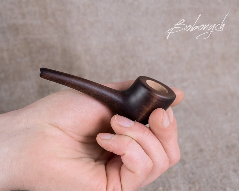 May include: A dark brown wooden pipe with a round bowl and a long, curved stem.