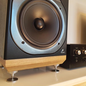 May include: A pair of black speakers with silver accents and a black amplifier with multiple knobs. The speakers have a wooden base and sit on silver feet. The amplifier is positioned between the speakers.
