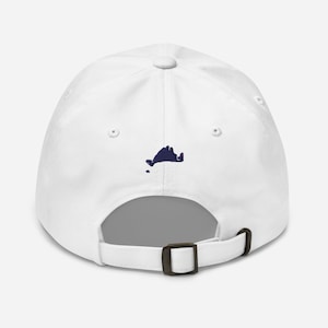 Könnte beinhalten: Eine weiße Baseballkappe mit einem dunkelblauen, gestickten Design einer Landmasse auf der Rückseite. Die Kappe hat einen gebogenen Schirm, einen Metallverschluss und einen Knopf oben.