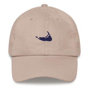 Può includere: Un cappello da baseball beige con un contorno di un'isola ricamato in blu scuro.