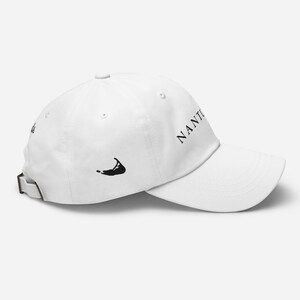 Può includere: Cappellino da baseball bianco con un contorno nero dell'isola di Nantucket e la parola "NANTUCKET" in testo nero.