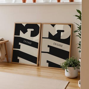 Puede incluir: Dos impresiones artísticas enmarcadas con una combinación de colores negro y crema, con la palabra "CHICAGO" y el número "72" en una fuente audaz y moderna. Las impresiones están apoyadas contra una pared en una habitación con un taburete de madera y plantas.