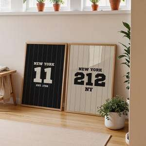Puede incluir: Dos impresiones enmarcadas con el texto "NEW YORK" y los números 11 y 212, en una habitación con un taburete de madera y plantas. La primera impresión es negra con texto blanco y rayas finas. La segunda es beige con texto negro y rayas finas.