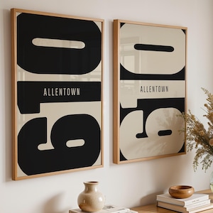 May include: Two framed art prints with a bold black and cream design. Each print features the word "ALLENTOWN" in a white font. The frames are made of light-colored wood. The prints are hanging on a white wall.