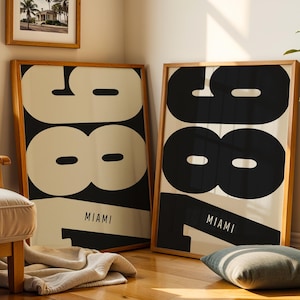 Puede incluir: Dos láminas enmarcadas con un diseño minimalista. Cada lámina presenta el número "1987" en letras negras grandes sobre un fondo crema, con "MIAMI" impreso debajo. Los marcos son de madera clara.