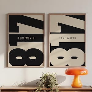 May include: Two framed art prints with a minimalist design. Each print features the number "18" in black and off-white, with "FORT WORTH" in a black sans-serif font. The prints are displayed on a wooden dresser.