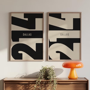 Könnte beinhalten: Zwei gerahmte Kunstdrucke mit minimalistischem Design. Jeder Druck zeigt das Wort "DALLAS" in einem rechteckigen Block mit großen abstrakten schwarzen und weißen Zahlen. Die Rahmen sind hellholzfarben.