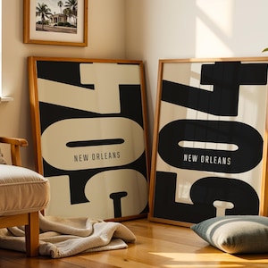 May include: Two framed art prints with a minimalist design. Each print features the number "704" in large, bold black letters against a cream background, with "NEW ORLEANS" printed below. The frames are made of light-colored wood.