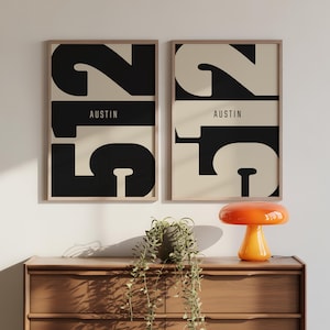 Puede incluir: Dos láminas enmarcadas con un diseño minimalista. Cada lámina presenta el número "2516" en negro y beige, con la palabra "AUSTIN" en el centro. Una lámpara de seta naranja se encuentra sobre una cómoda de madera.