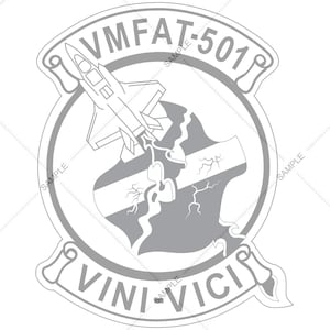 May include: A gray and white emblem featuring a jet aircraft taking off, with the text "VMFAT-501" at the top and "VINI VICI" at the bottom. The emblem has a circular design with a shield-like shape in the center.