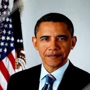 Puede incluir: Un retrato de un hombre con un traje oscuro, una camisa azul claro y una corbata a rayas azul y blanca. Lleva un pequeño pin de la bandera estadounidense en la chaqueta de su traje. El fondo es una imagen borrosa de una bandera estadounidense.