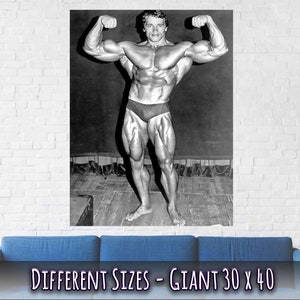 Op de afbeelding: Zwart-witfoto van een bodybuilder die zijn biceps aanspant. De foto is afgedrukt op een poster met de tekst "DIFFERENT SIZES - GIANT 30 x 40".