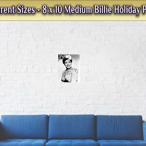 May include: A black and white photo of Billie Holiday, a famous jazz singer, wearing a floral hat and a dress. The photo is framed and hanging on a white brick wall.