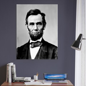 a portrait of Abraham Lincoln, a famous American president, hanging on a wall above a wooden desk with a laptop, books, and other office supplies.