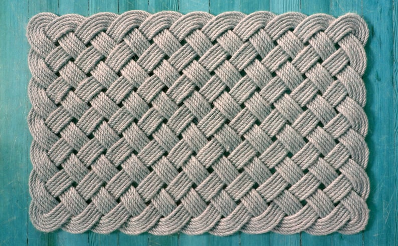 May include: A gray woven doormat with a diamond pattern. The mat is made of thick rope and has a slightly rounded edge.