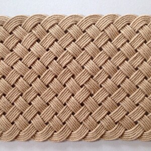 May include: A natural fiber doormat woven in a basket weave pattern with a decorative edge. The mat is beige in color.